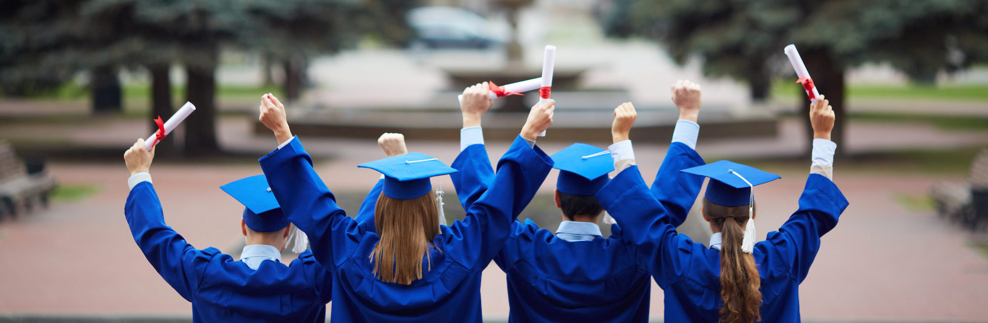 Backs of ecstatic students in graduation gowns holding diplomas